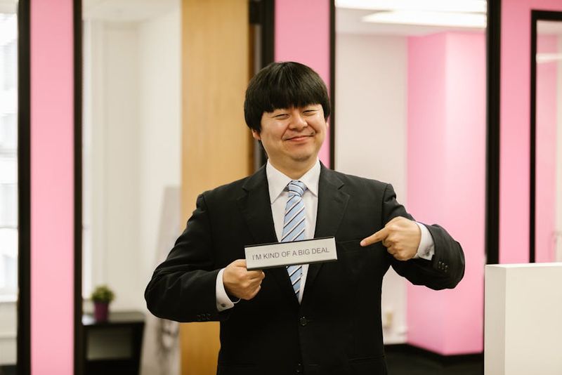 Asian businessman confidently holding funny office sign, showcasing humor in business attire.
