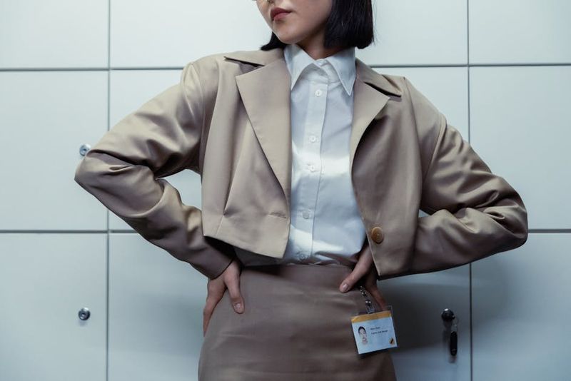 Primo piano di una donna d'affari con le mani sui fianchi, che indossa un badge identificativo e una giacca.