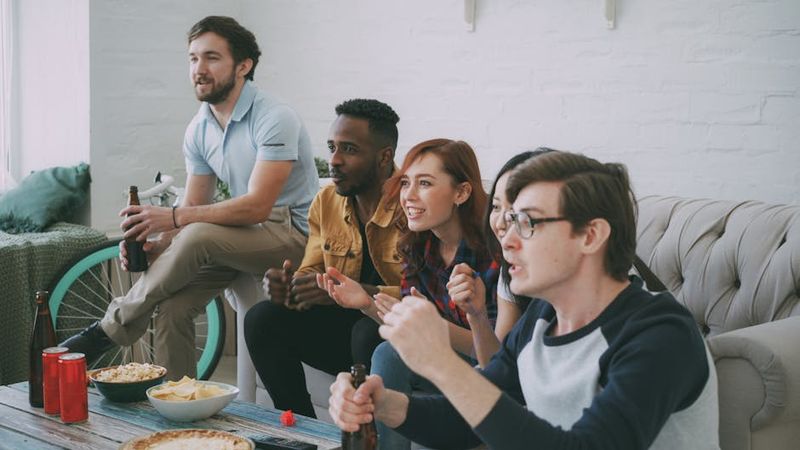 A diverse group of friends enjoying a sports game indoors with snacks and drinks.