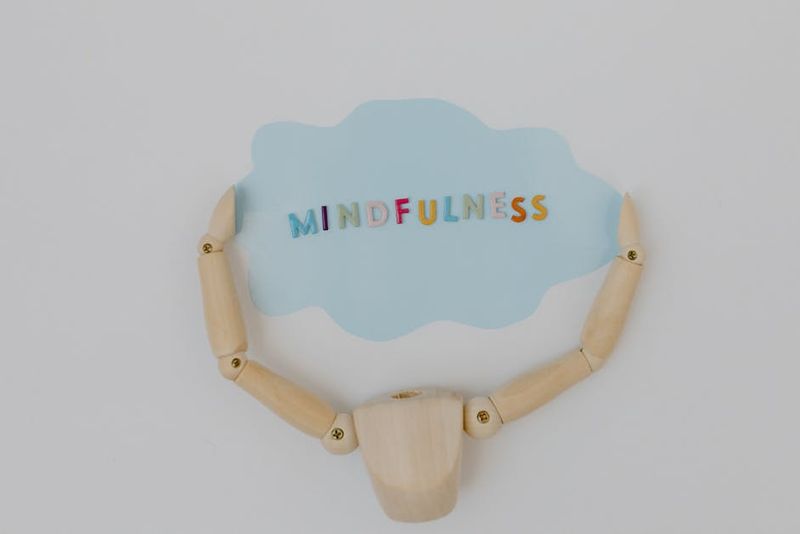 Wooden mannequin arms holding a blue cloud with 'Mindfulness' text, promoting self-awareness.