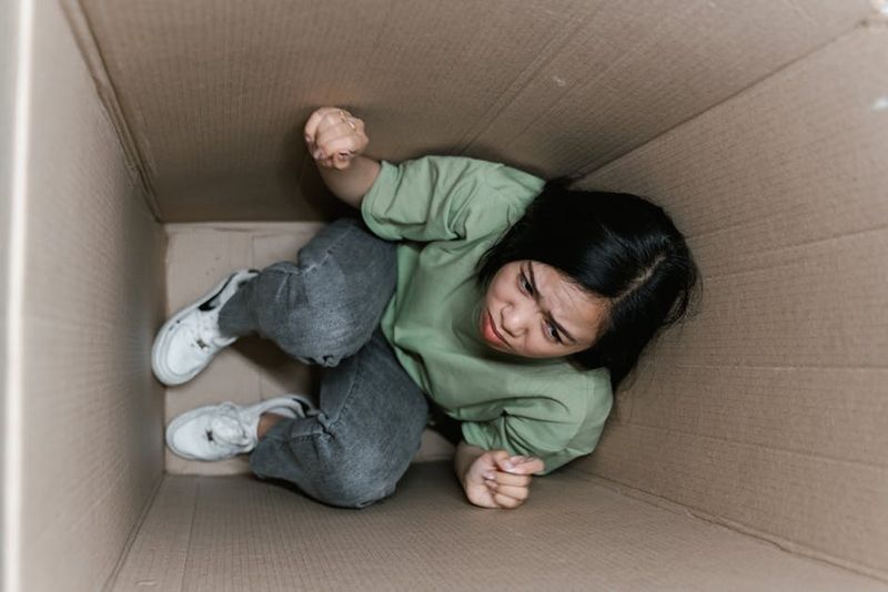 Uma mulher se sentindo presa e ansiosa dentro de uma pequena caixa de papelão, simbolizando claustrofobia.