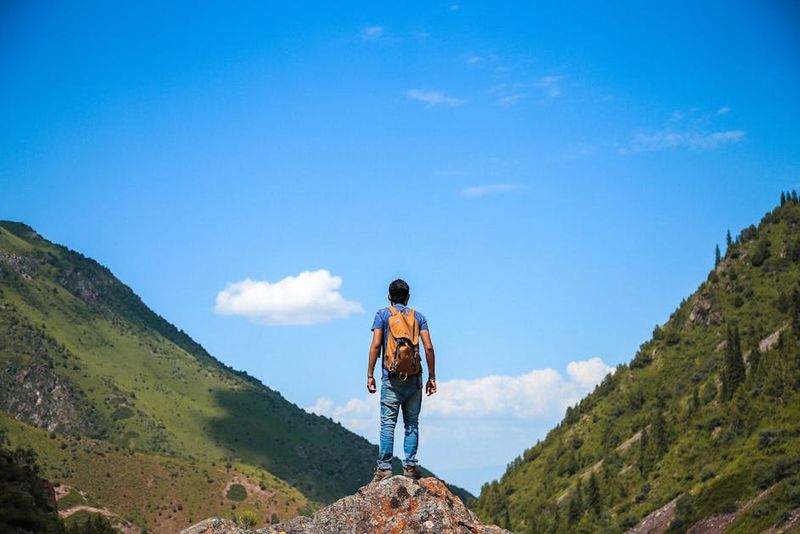 A solo backpacker standing on a rock, admiring the mountain view under a bright blue sky.