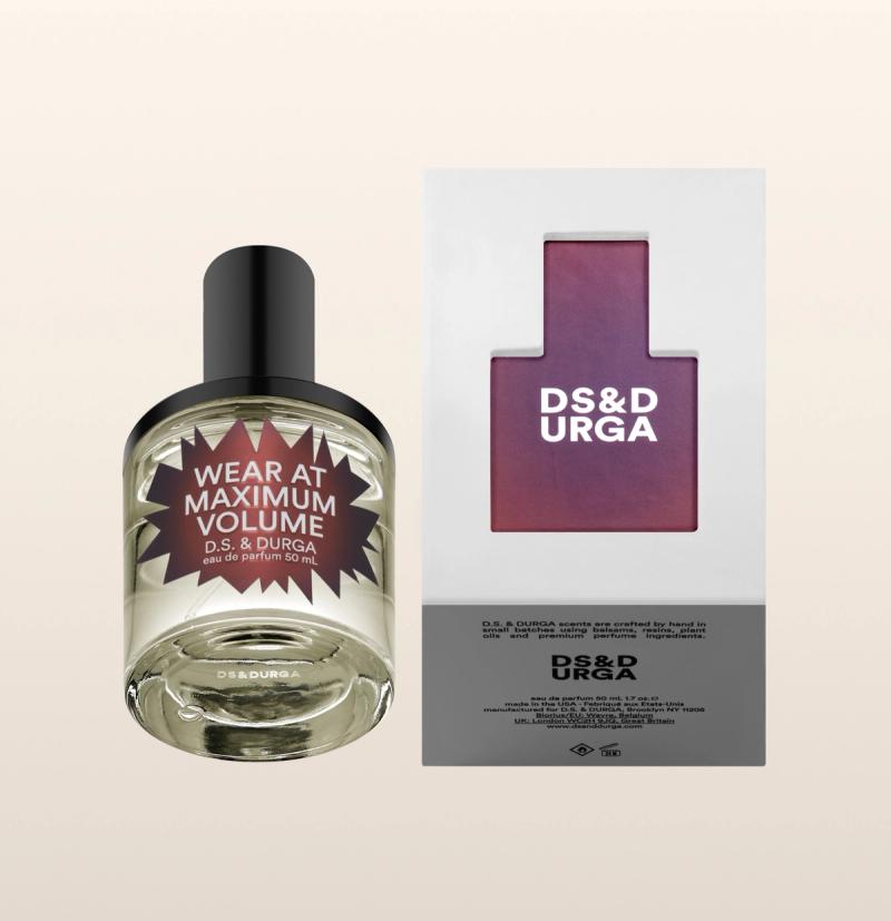 A bottle of D.S. & Durga perfume labeled "Wear at Maximum Volume" next to its packaging. The box has a cut-out in the shape of a bottle, displaying the brand name.