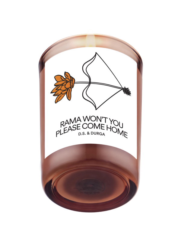 A lit scented candle featuring an illustration of a flower and a kite, and the text "rama, won't you please come home" by d.s. & durga.