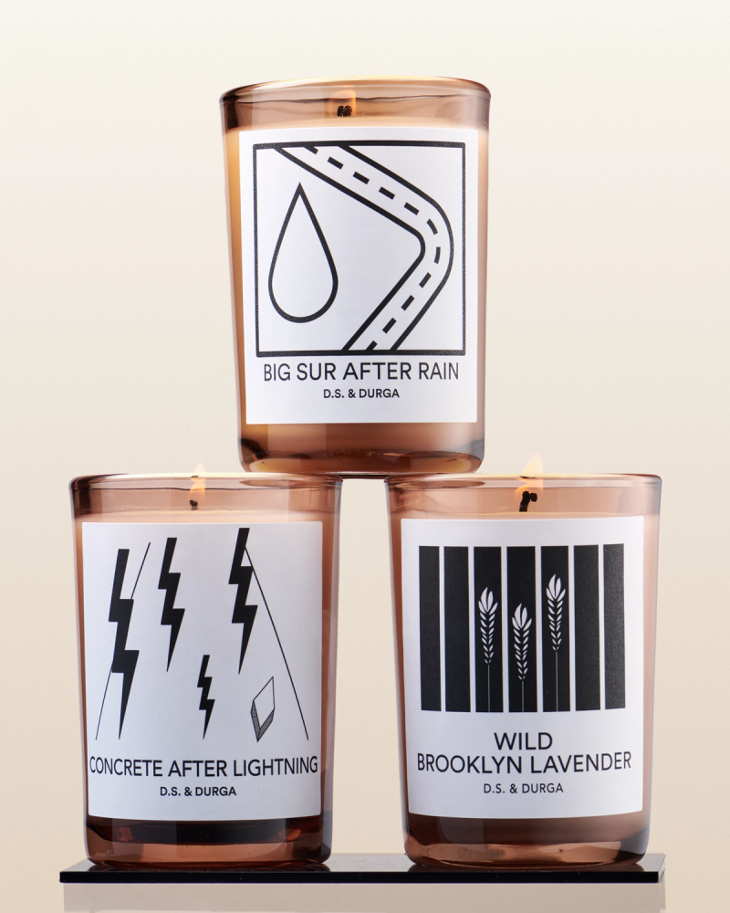 Three luxury scented candles with distinct themes displayed in an elegant arrangement: "big sur after rain," "concrete after lightning," and "wild brooklyn lavender.