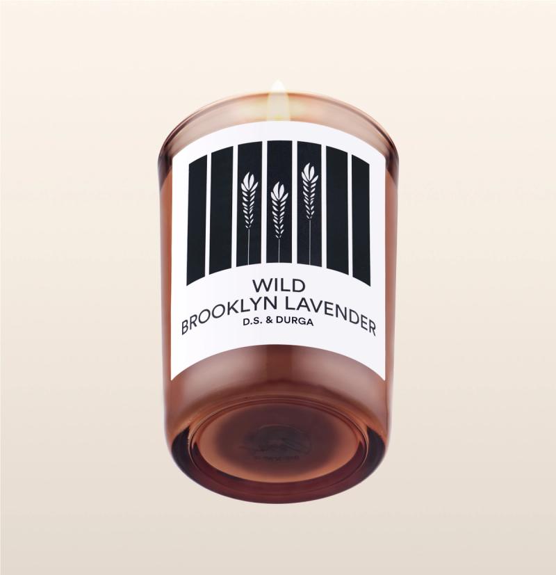 A lit scented candle with label reading "wild brooklyn lavender" label by d.s. &amp; durga on a transparent background.
