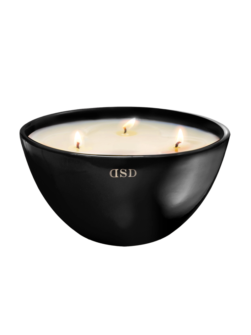 A large, black bowl-shaped candle with three lit wicks, creating a tranquil and aromatic ambiance.