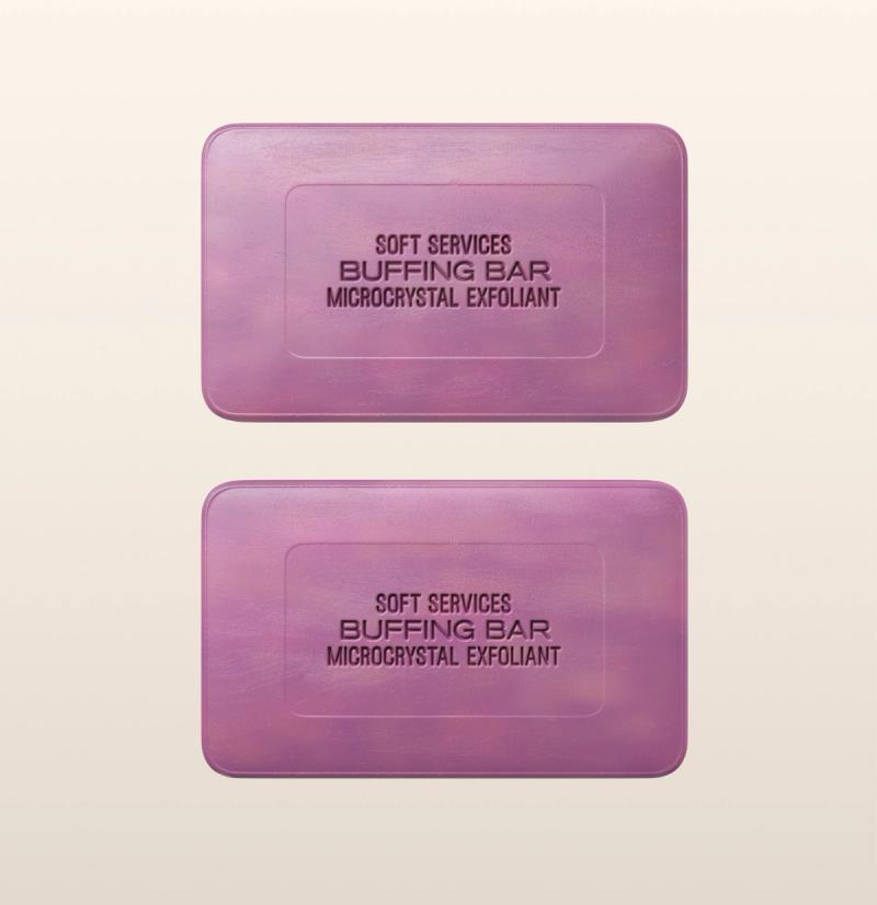 Two purple rectangular bars labeled "Soft Services Buffing Bar Microcrystal Exfoliant" are displayed on a light beige background. The bars appear smooth with slightly rounded edges and are positioned one above the other.