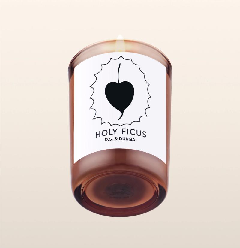A lit scented candle with a label reading "holy ficus" d.s. &amp; durga on a transparent background.