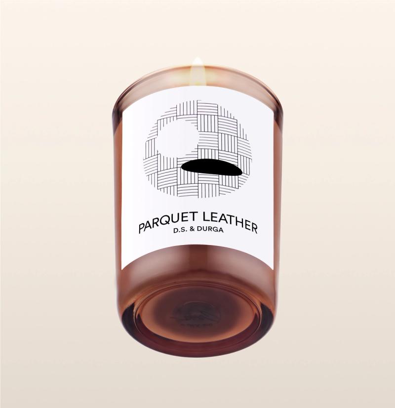 A lit scented candle with the label "parquet leather d.s. &amp; durga" on a transparent background.