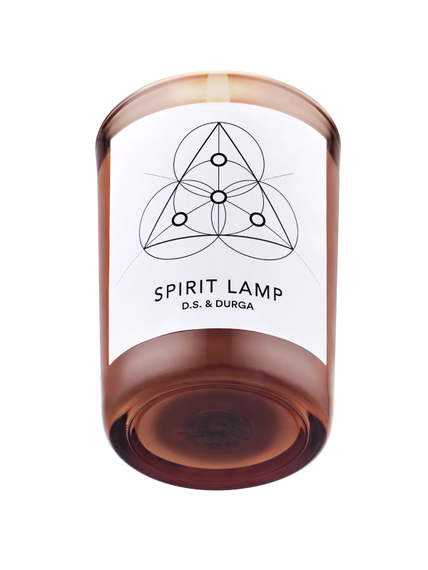 A lit scented candle with a label that reads "spirit lamp" by d.s. &amp; durga, featuring a geometric pattern. 