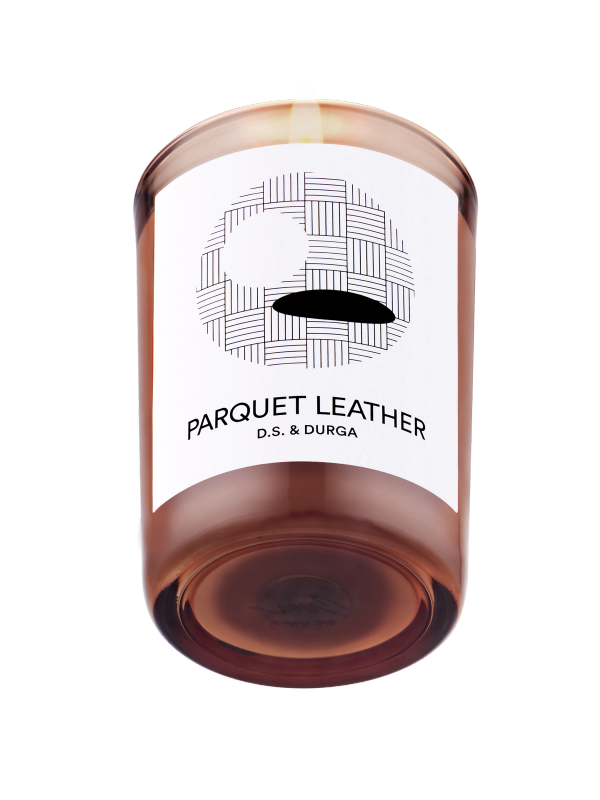 A lit scented candle with the label "parquet leather d.s. &amp; durga" on a transparent background.