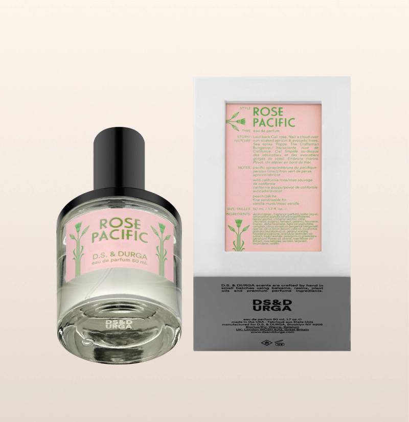 A bottle of D.S. &amp; Durga Rose Pacific eau de parfum stands beside its box. Both feature minimalist, pale pink and green labels with floral accents and product details. The background is a soft beige gradient.