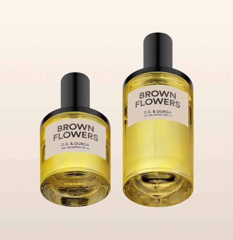 Two perfume bottles of "Brown Flowers" by D.S. &amp; Durga are displayed against a light background. The larger bottle is labeled "eau de parfum 100 ml" and the smaller "eau de parfum 50 ml." Both have black caps and amber-colored liquid inside.