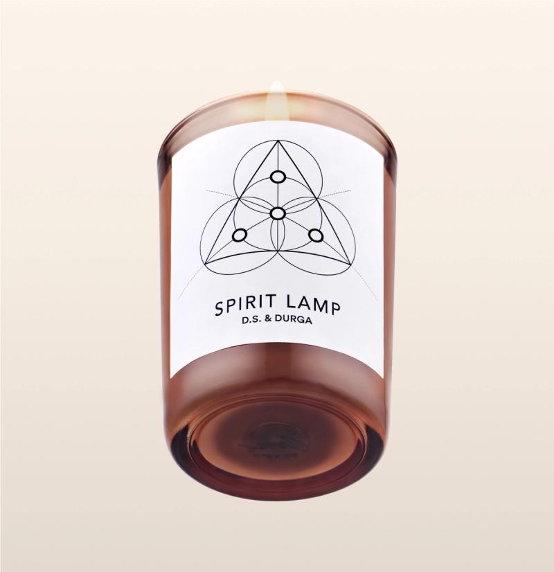 A lit scented candle with a label that reads "spirit lamp" by d.s. &amp; durga, featuring a geometric pattern. 