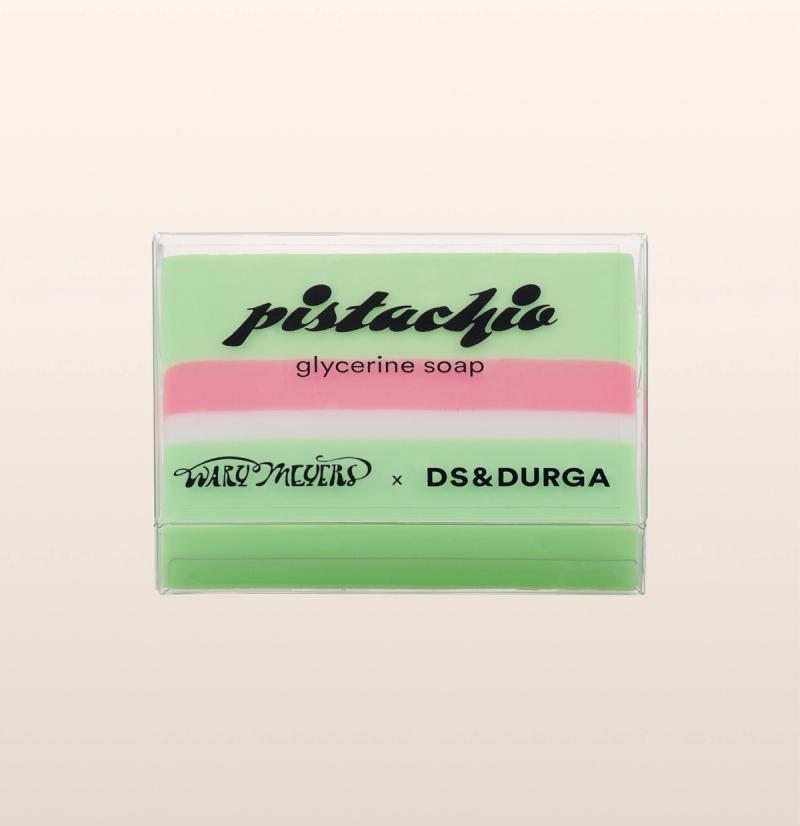 A bar of pistachio glycerine soap in translucent packaging with green and pink layers, featuring a collaboration between brands Wary Meyers and D.S. & Durga.