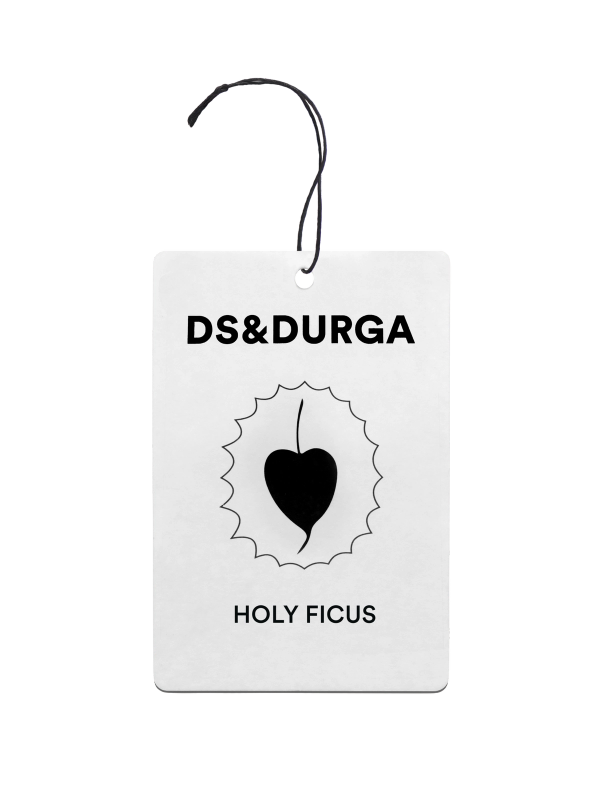 A hanging auto fragrance with the inscription "ds&durga" at the top and the name "holy ficus" below an emblem featuring a leaf silhouette inside a jagged circle. 