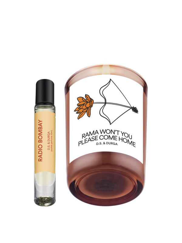 A perfume roller labeled "Radio Bombay" stands next to a lit candle in a glass holder labeled "Rama Won't You Please Come Home" with a bow and flower illustration; both are D.S. & Durga products.