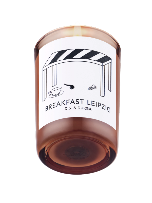 A lit scented candle labeled "breakfast leipzig" by d.s. &amp; durga, showcasing minimalist packaging design on a transparent background.