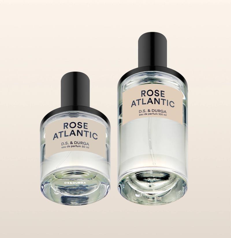 Two clear glass perfume bottles labeled "ROSE ATLANTIC" by D.S. & Durga, one smaller (50 ml) and one larger (100 ml), both with black caps and a beige label, set against a light gradient background.