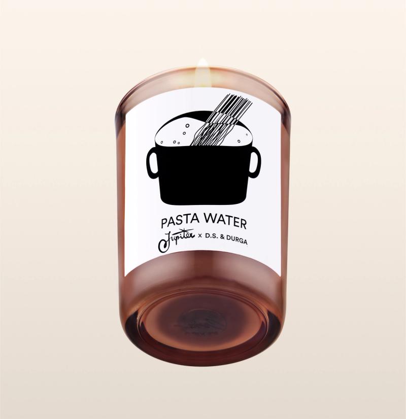 A lit scented candle with label reading "pasta water" by jupiter &amp; d.s. &amp; durga, featuring an illustration of a pot with steam rising, set against a transparent background.