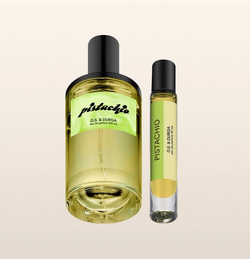 Two bottles of D.S. & Durga Pistachio perfume are shown against a light beige background: one large and one small, both cylindrical with black caps and yellow-green liquid inside.