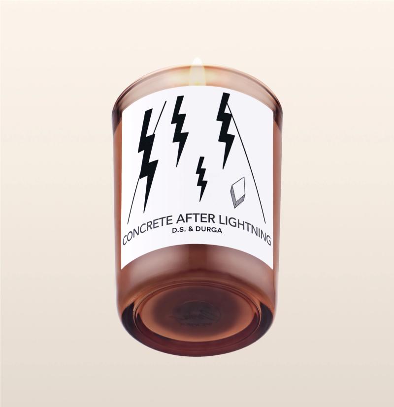 A lit scented candle labeled "concrete after lightning" by d.s. &amp; durga, featuring a minimalist label design with lightning bolt graphics.