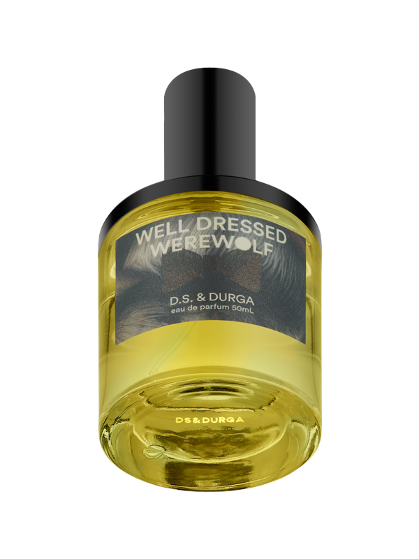 A bottle of D.S. &amp; Durga perfume labeled "WELL DRESSED WEREWOLF" with yellow liquid inside and a black cap, featuring a dark, textured label design.