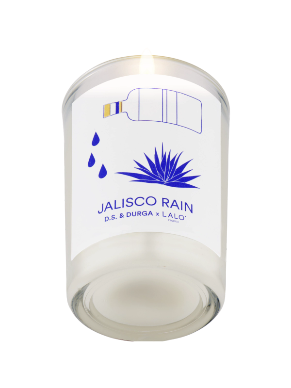 A lit candle in a clear glass holder is shown against a light background. The label reads "JALISCO RAIN D.S. & DURGA x LALO" in blue text, with illustrations of a bottle pouring liquid, water drops, and an agave plant.