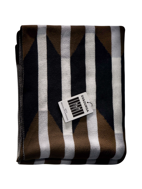 A brown, black, white, and gray woven cotton blanket with a geometric pattern, folded into a rectangle, with a DS & Durga Wild Brooklyn Lavender auto fragrance resting on top of it.