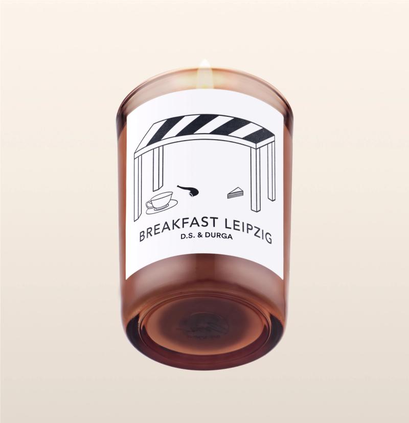 A lit scented candle labeled "breakfast leipzig" by d.s. &amp; durga, showcasing minimalist packaging design on a transparent background.