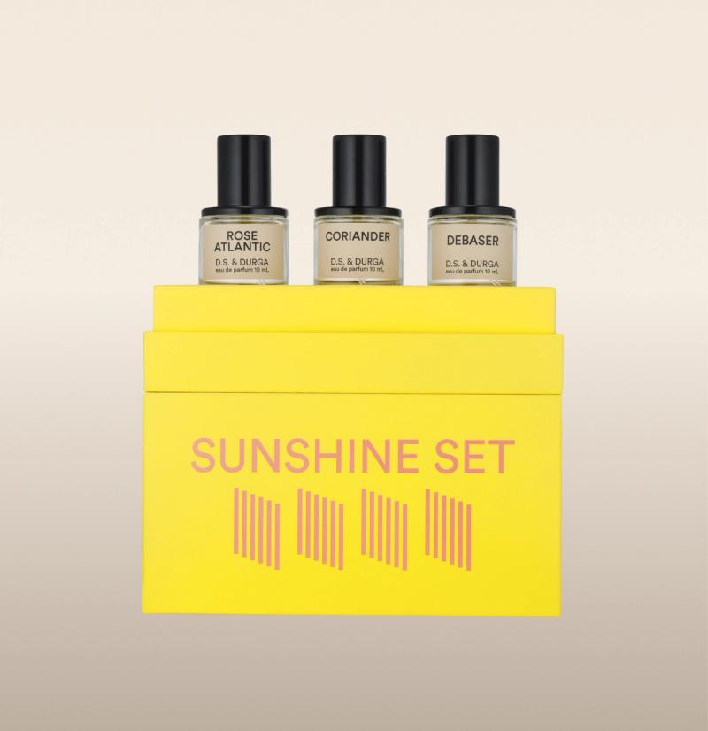 A bright yellow box labeled "Sunshine Set" contains three perfume bottles. The bottles are individually labeled: "Rose Atlantic," "Coriander," and "Debaser." Each bottle is labeled "D.S. & Durga eau de parfum 10 mL.