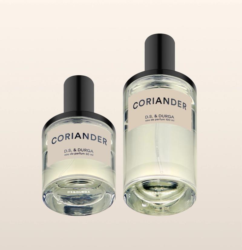 Two clear glass bottles of D.S. & Durga Coriander eau de parfum, one smaller (50 ml) and one larger (100 ml), each with a black cap and light beige label, displayed on a pale gradient background.