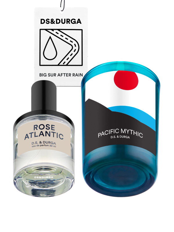 Three D.S. & Durga products: a Rose Atlantic perfume bottle, a blue Pacific Mythic candle with a graphic label, and a Big Sur After Rain car air freshener with a raindrop icon and hanging string.