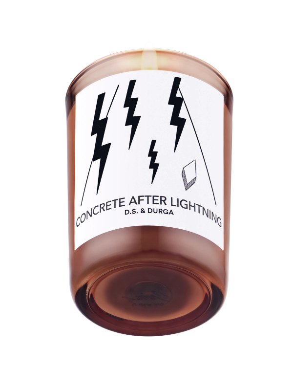 A lit scented candle labeled "concrete after lightning" by d.s. &amp; durga, featuring a minimalist label design with lightning bolt graphics.