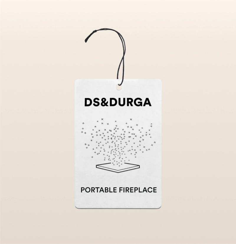 A hanging auto fragrance with the inscription"ds & durga" on the upper portion and "portable fireplace" below, featuring a stylized graphic of sparkles dispersing above an open book.