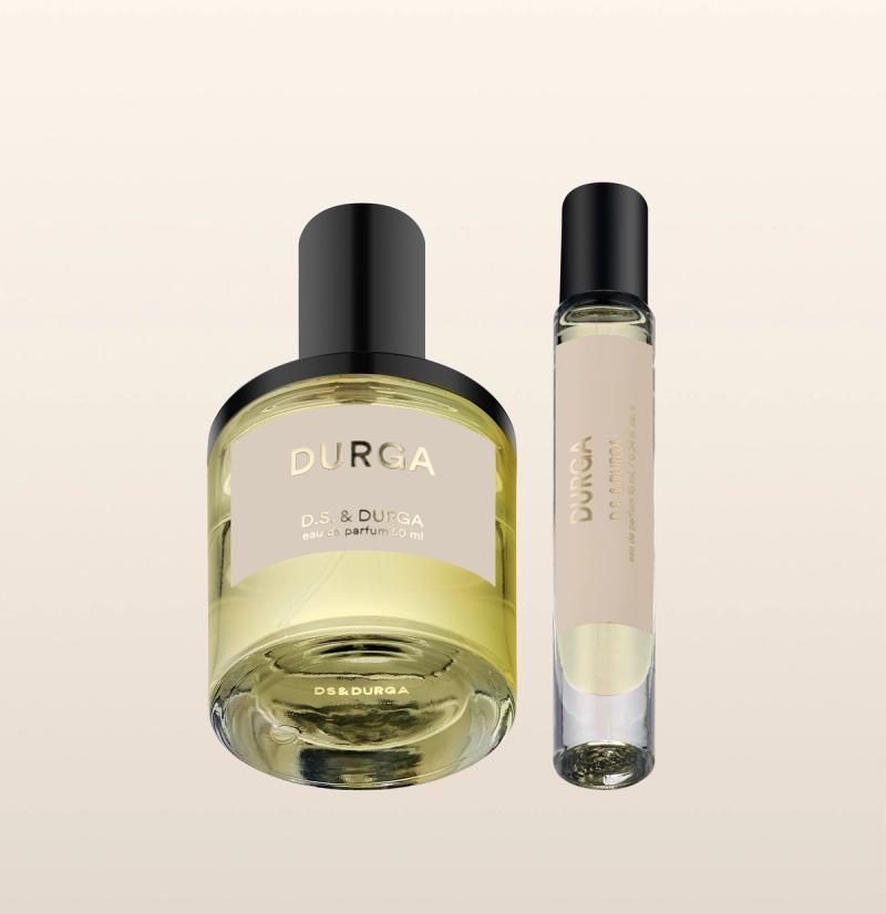 A large and a small bottle of D.S. &amp; Durga perfume are shown against a light beige background. The larger bottle has a round body and black cap; the smaller, a slim cylindrical shape with a black cap.