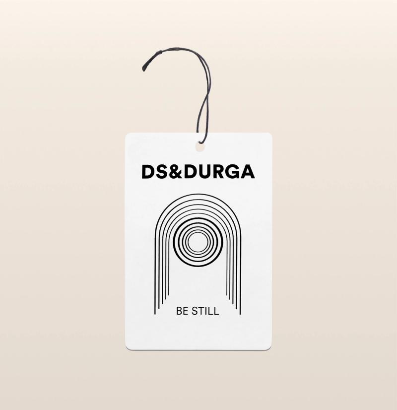 A DS & DURGA air freshener featuring a minimalist black line design on a cream background with the text "BE STILL" underneath, along with a black string for hanging.