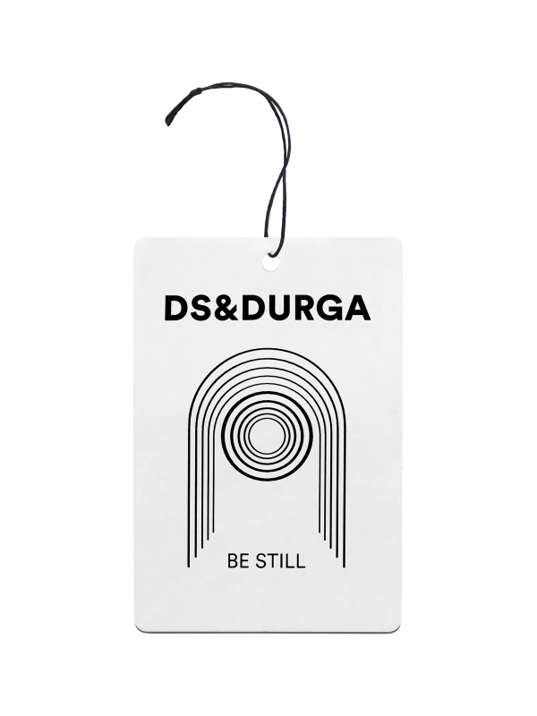 A DS & DURGA air freshener featuring a minimalist black line design on a white background with the text "BE STILL" underneath, along with a black string for hanging.