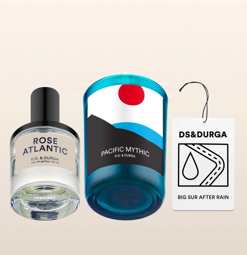 Three D.S. &amp; Durga products: a Rose Atlantic perfume bottle, a blue Pacific Mythic candle with a graphic label, and a Big Sur After Rain car air freshener with a raindrop icon and hanging string.
