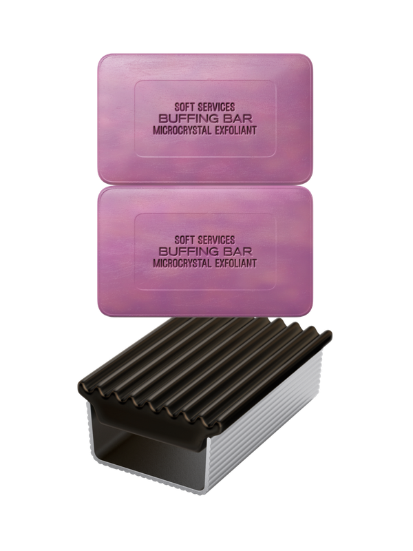 Two rectangular pink bars labeled "Soft Services Buffing Bar Microcrystal Exfoliant" are positioned above a dark purple and white ribbed soap holder. The bars are stacked one on the other, with the soap holder placed beneath.