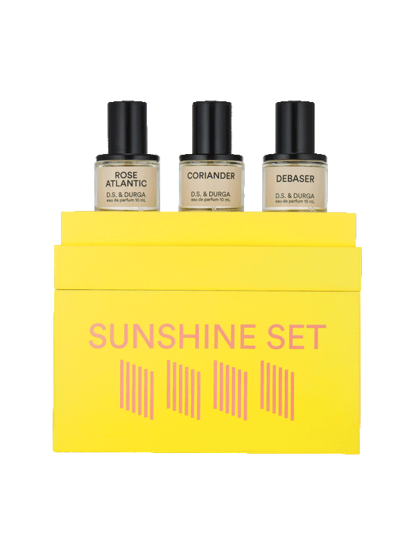 A bright yellow box labeled "Sunshine Set" contains three perfume bottles. The bottles are individually labeled: "Rose Atlantic," "Coriander," and "Debaser." Each bottle is labeled "D.S. & Durga eau de parfum 10 mL.