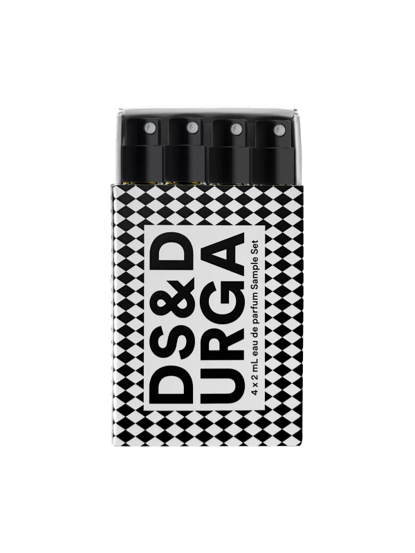 An artistic display of four cylindrical bottles with spray nozzles, emerging from a torn paper with the text "ds &amp; durga" printed on it in a bold, abstract font.