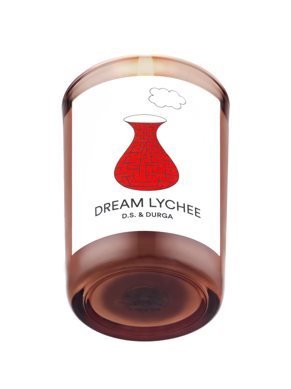 A lit scented candle with a warm, amber hue labeled "dream lychee" by d.s. &amp; durga, featuring an artistic red sketch of a traditional vase on its label.