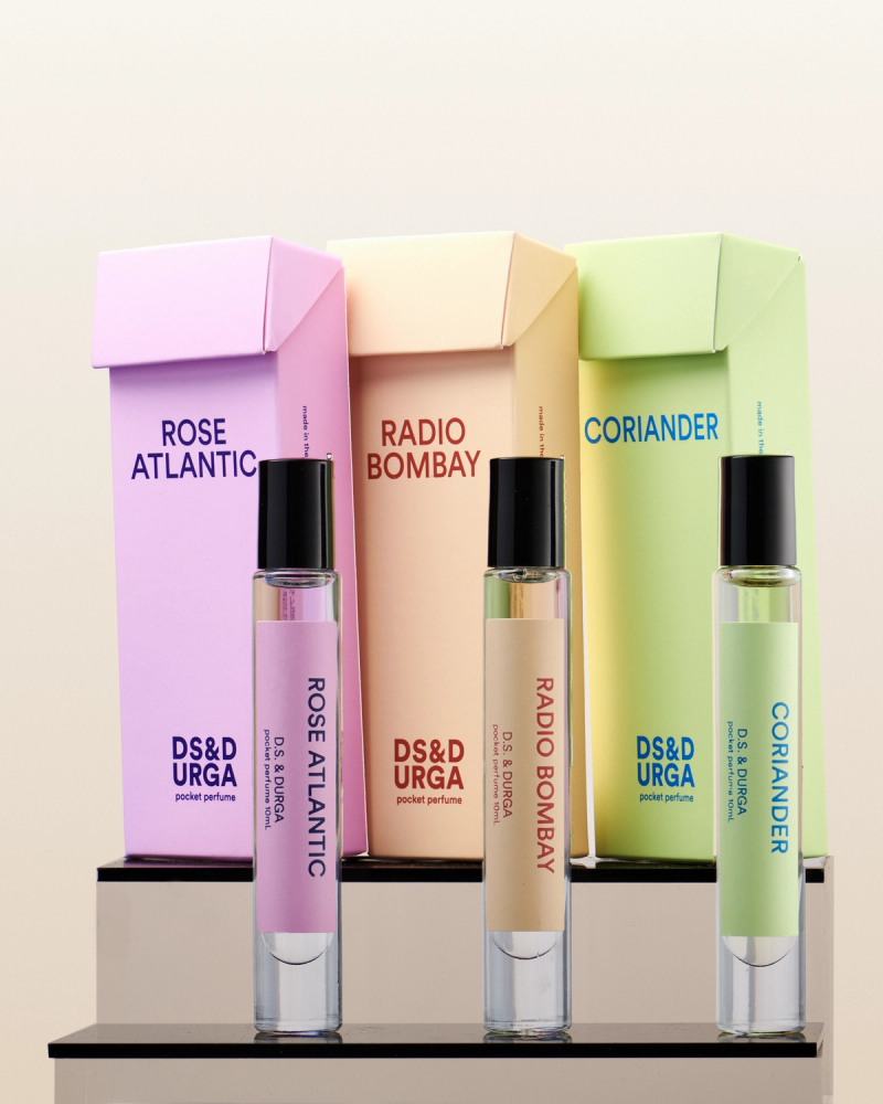 A collection of three sleek, travel-sized perfume bottles in front of their corresponding colorful boxes, each with a unique scent label: rose atlantic, radio bombay, and coriander.