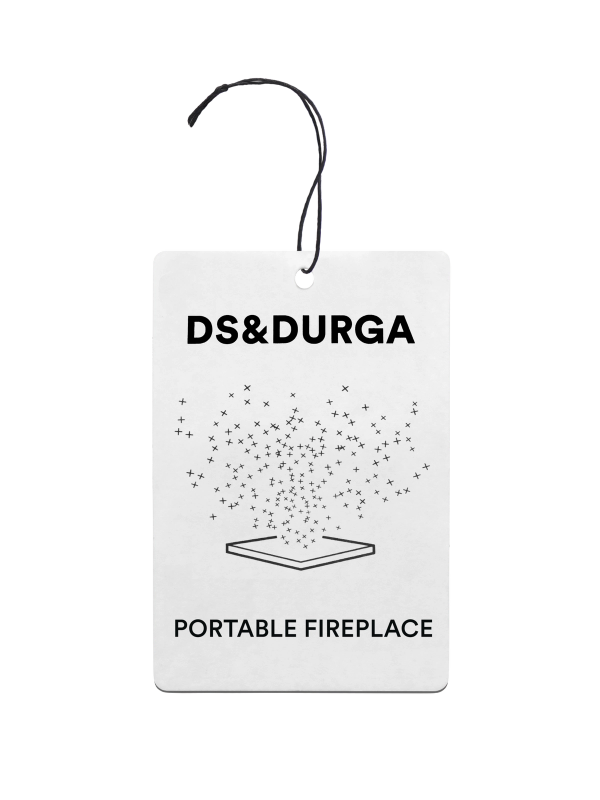 A hanging auto fragrance with the inscription"ds & durga" on the upper portion and "portable fireplace" below, featuring a stylized graphic of sparkles dispersing above an open book.