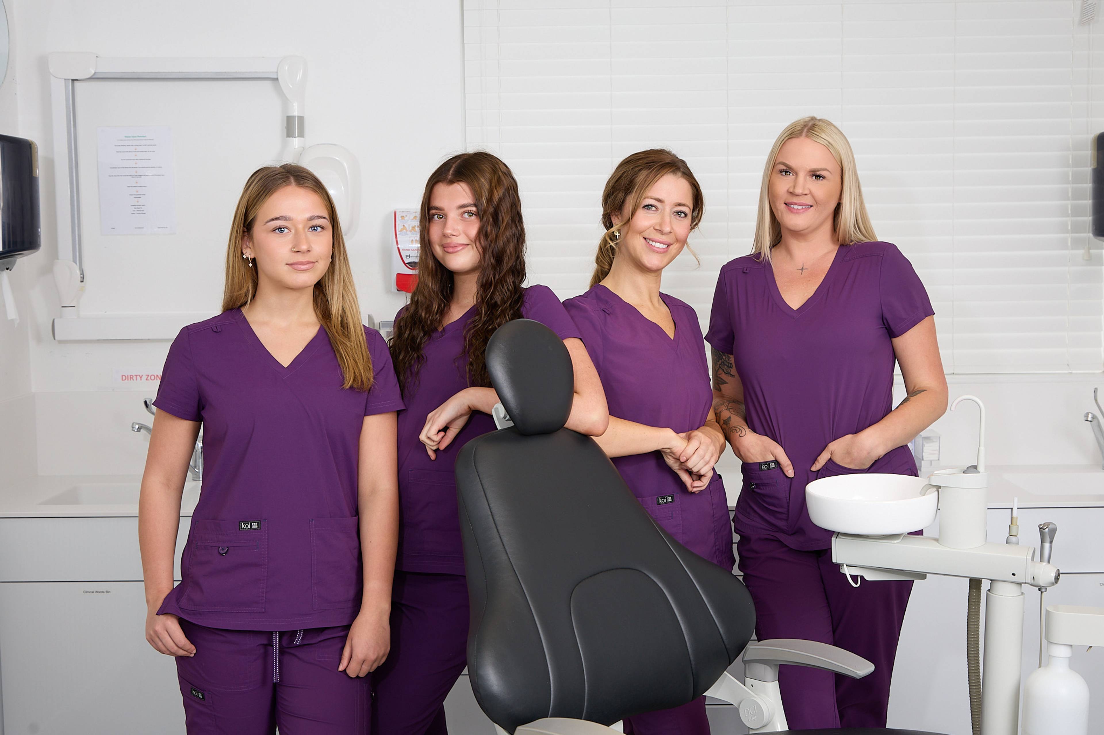 Four of our dental therapists stand in a treatment room wearing purple uniforms