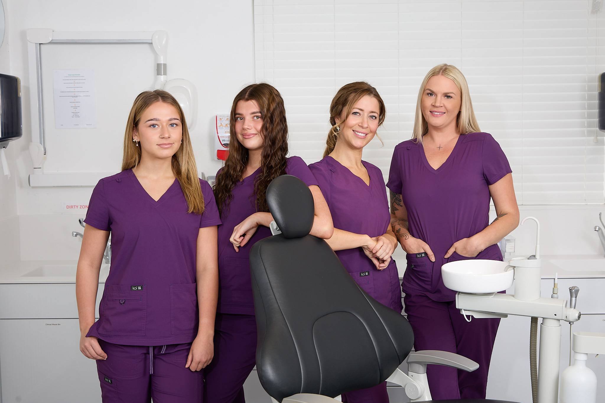 Four of our dental therapists stand in a treatment room wearing purple uniforms