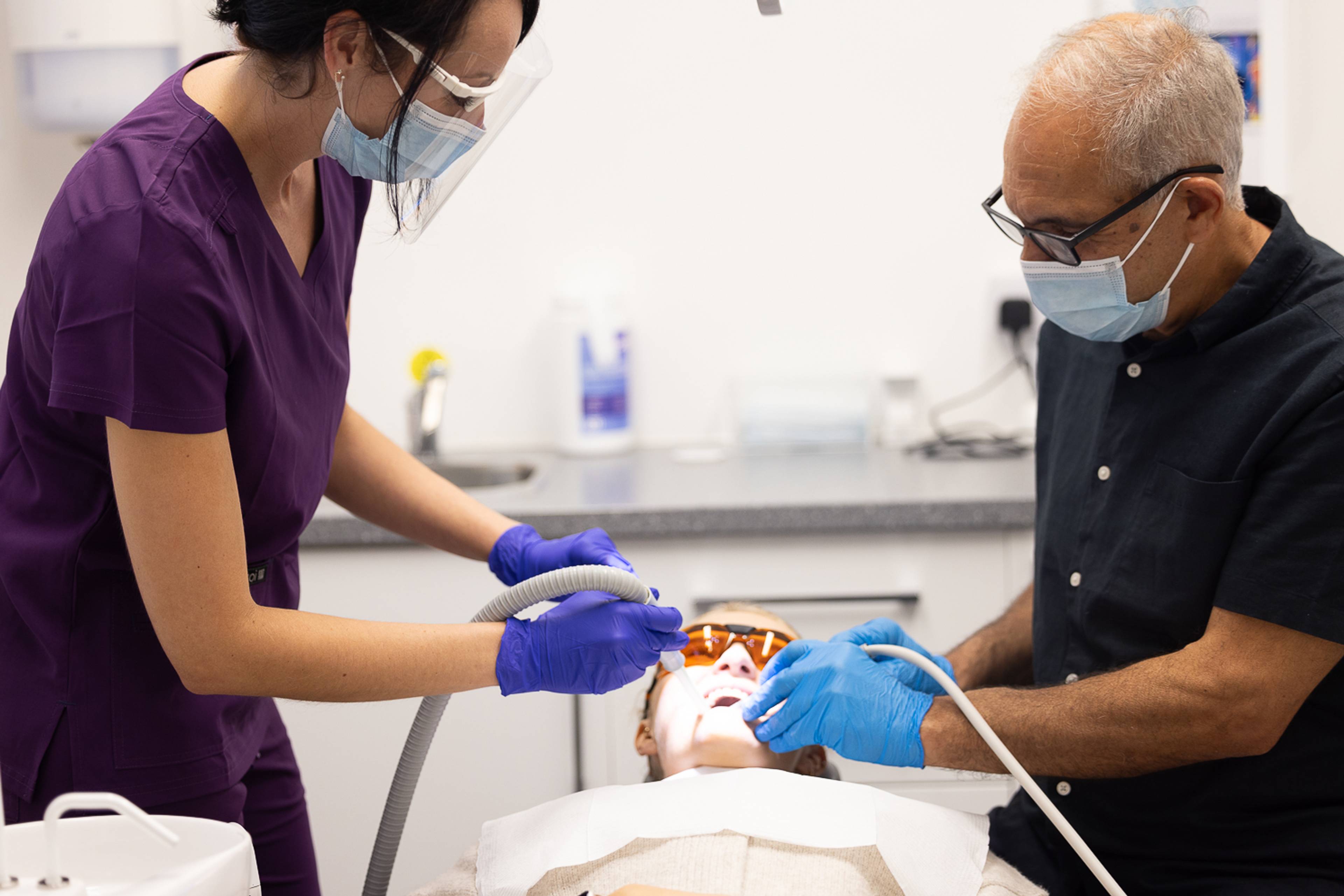 Dentist Shahriar Majlessi examining a patient's teeth with the help of dental therapist Lucy Steward