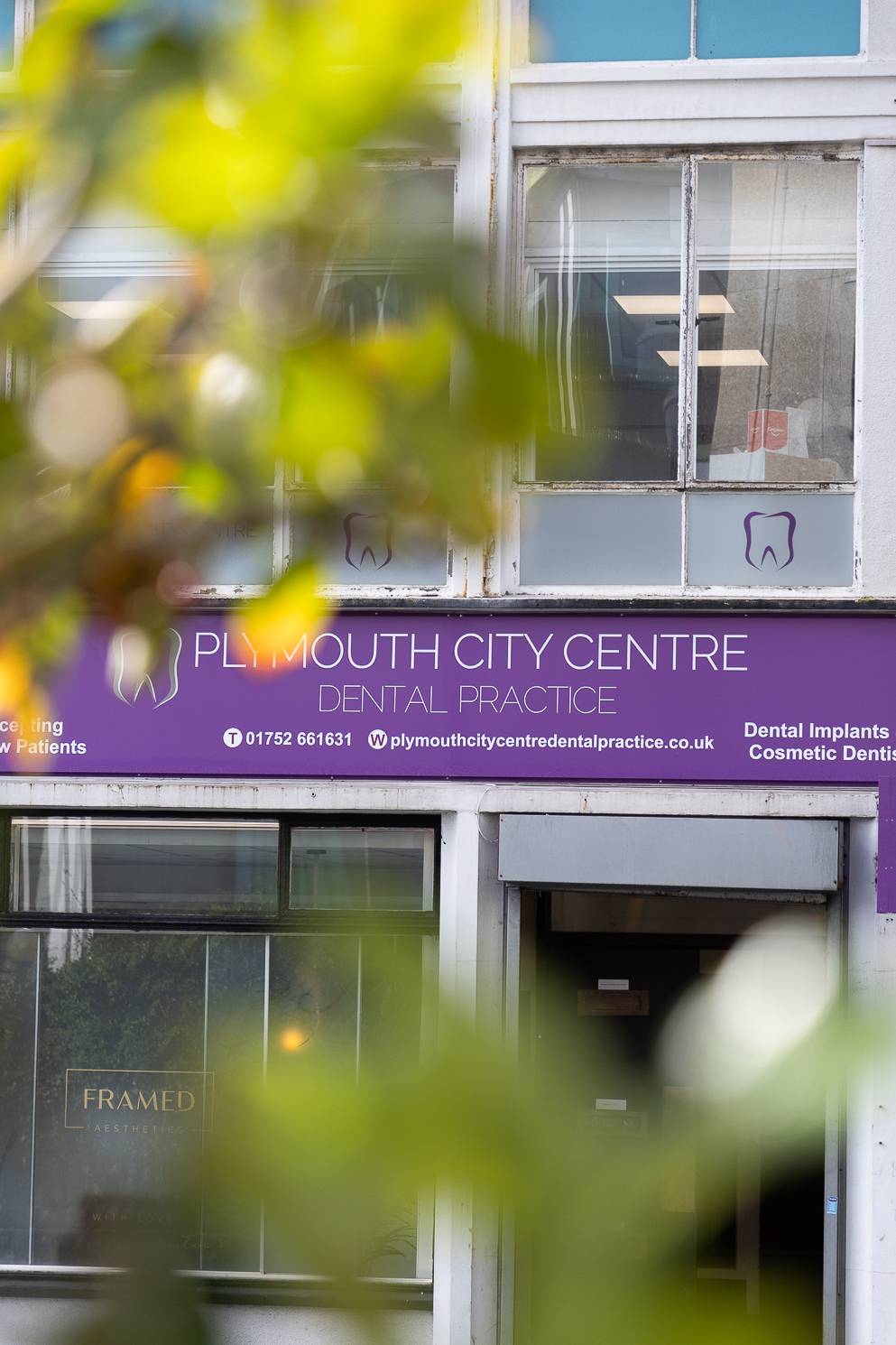 The front of the Plymouth City Centre Dental Practice clinic, partially obscured by out-of-focus trees in the foreground